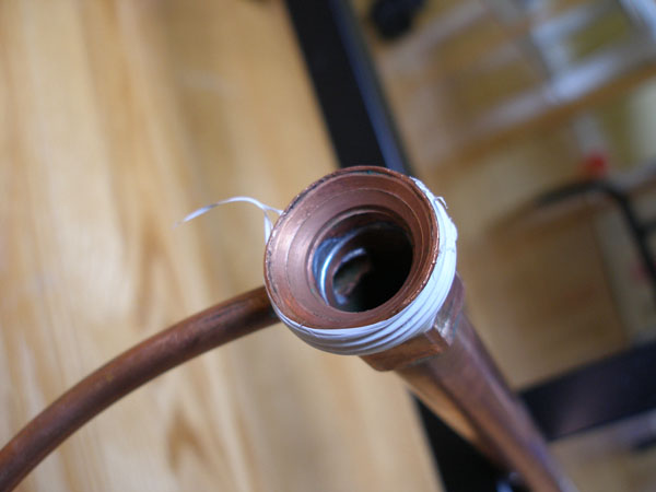 Hex-sided half of the coupling soldered to the long copper pipe, with the small copper inlet tube entering at an angle